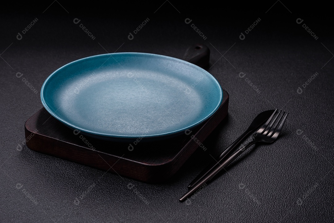 Linda placa cerâmica redonda vazia sobre um fundo de concreto. Utensílios de cozinha para servir comida na mesa