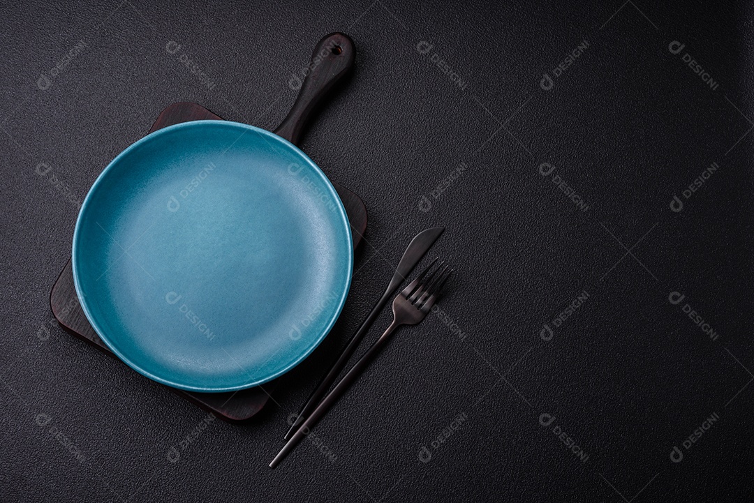 Linda placa cerâmica redonda vazia sobre um fundo de concreto. Utensílios de cozinha para servir comida na mesa