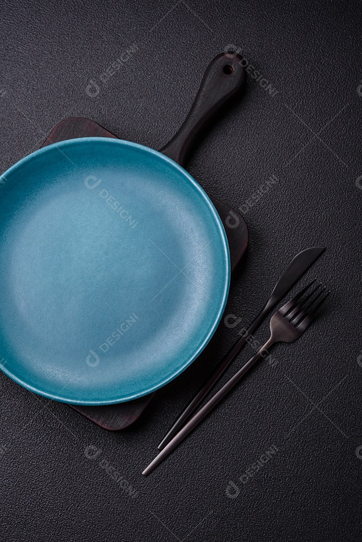 Linda placa cerâmica redonda vazia sobre um fundo de concreto. Utensílios de cozinha para servir comida na mesa
