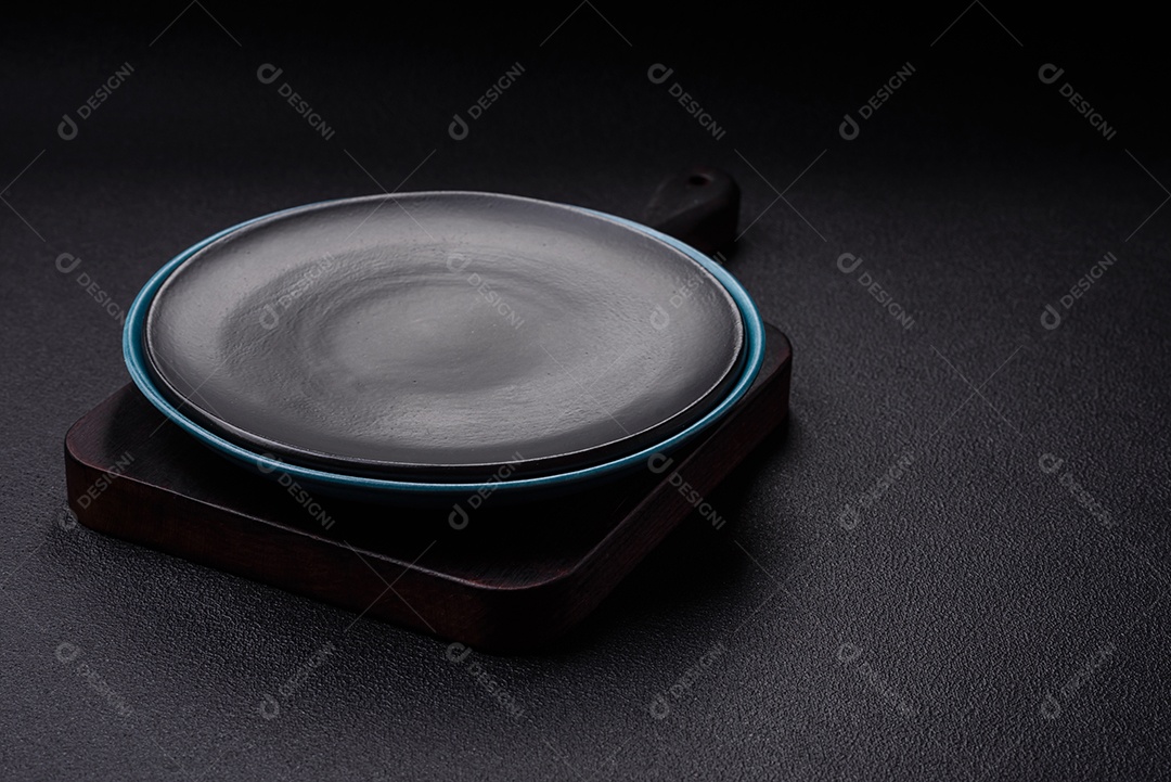 Linda placa cerâmica redonda vazia sobre um fundo de concreto. Utensílios de cozinha para servir comida na mesa