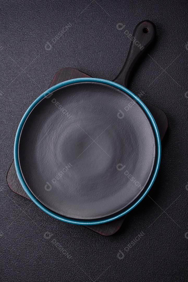 Linda placa cerâmica redonda vazia sobre um fundo de concreto. Utensílios de cozinha para servir comida na mesa