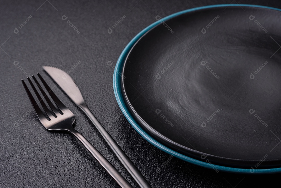 Linda placa cerâmica redonda vazia sobre um fundo de concreto. Utensílios de cozinha para servir comida na mesa