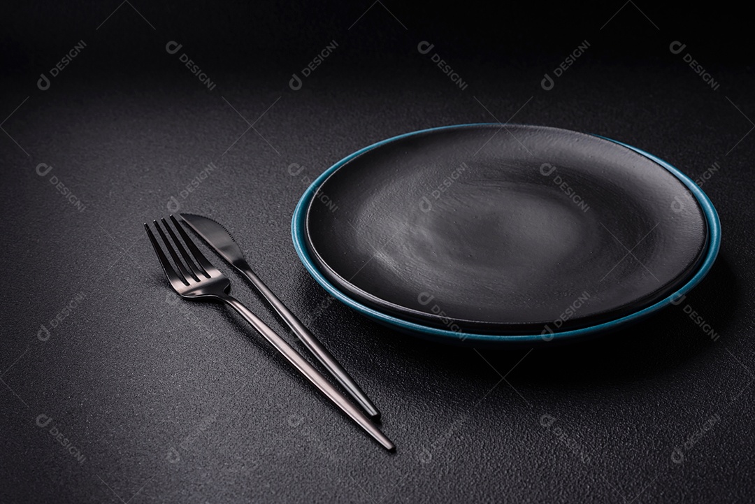 Linda placa cerâmica redonda vazia sobre um fundo de concreto. Utensílios de cozinha para servir comida na mesa