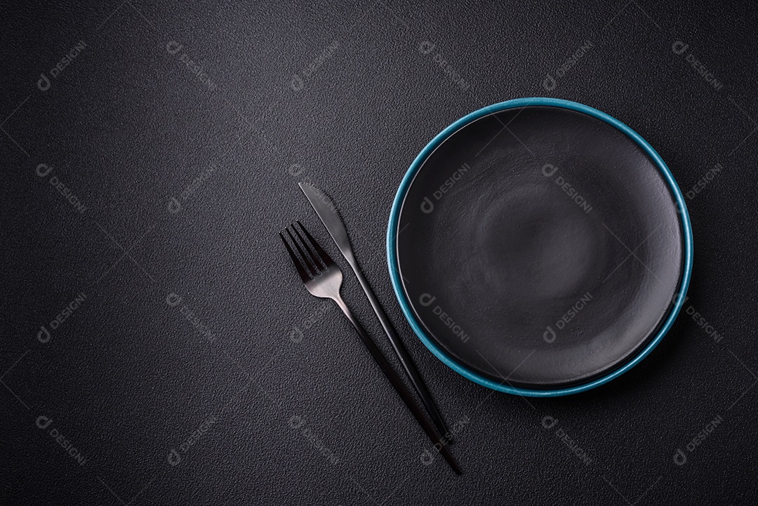 Linda placa cerâmica redonda vazia sobre um fundo de concreto. Utensílios de cozinha para servir comida na mesa