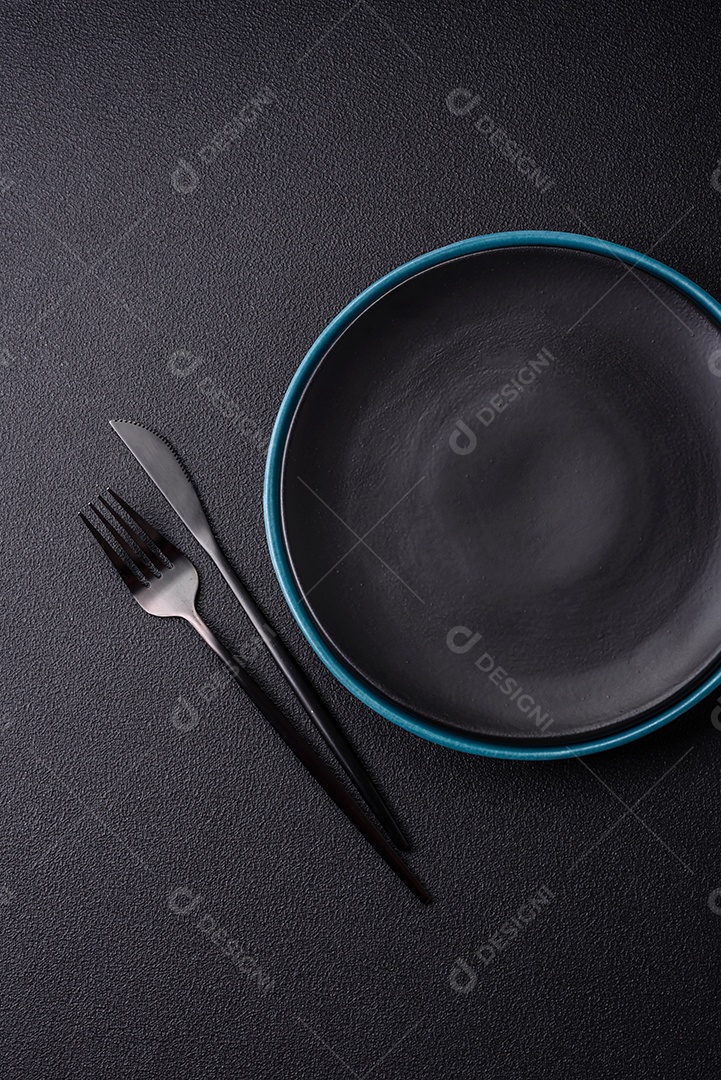 Linda placa cerâmica redonda vazia sobre um fundo de concreto. Utensílios de cozinha para servir comida na mesa