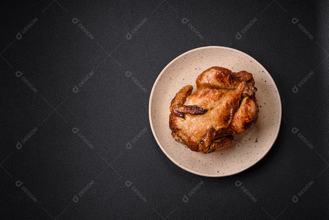 Frango assado inteiro delicioso e crocante com legumes, sal e especiarias sobre um fundo escuro de concreto