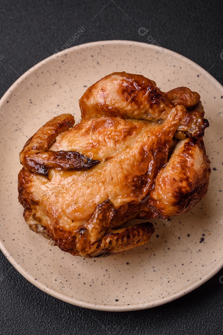 Frango assado inteiro delicioso e crocante com legumes, sal e especiarias sobre um fundo escuro de concreto