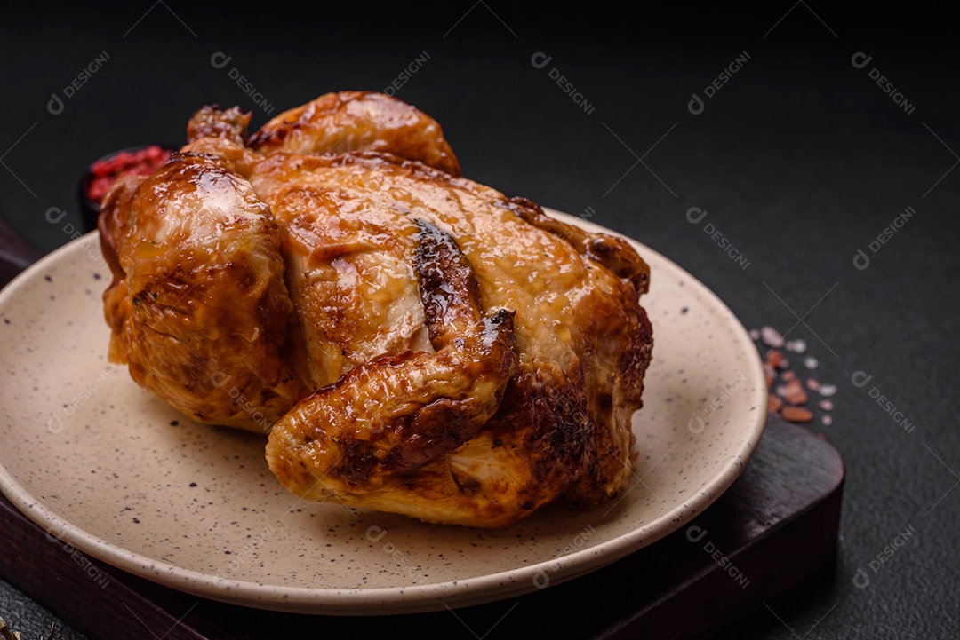 Frango assado inteiro delicioso e crocante com legumes, sal e especiarias sobre um fundo escuro de concreto