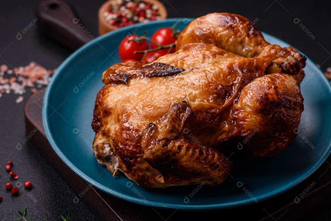 Frango assado inteiro delicioso e crocante com legumes, sal e especiarias sobre um fundo escuro de concreto