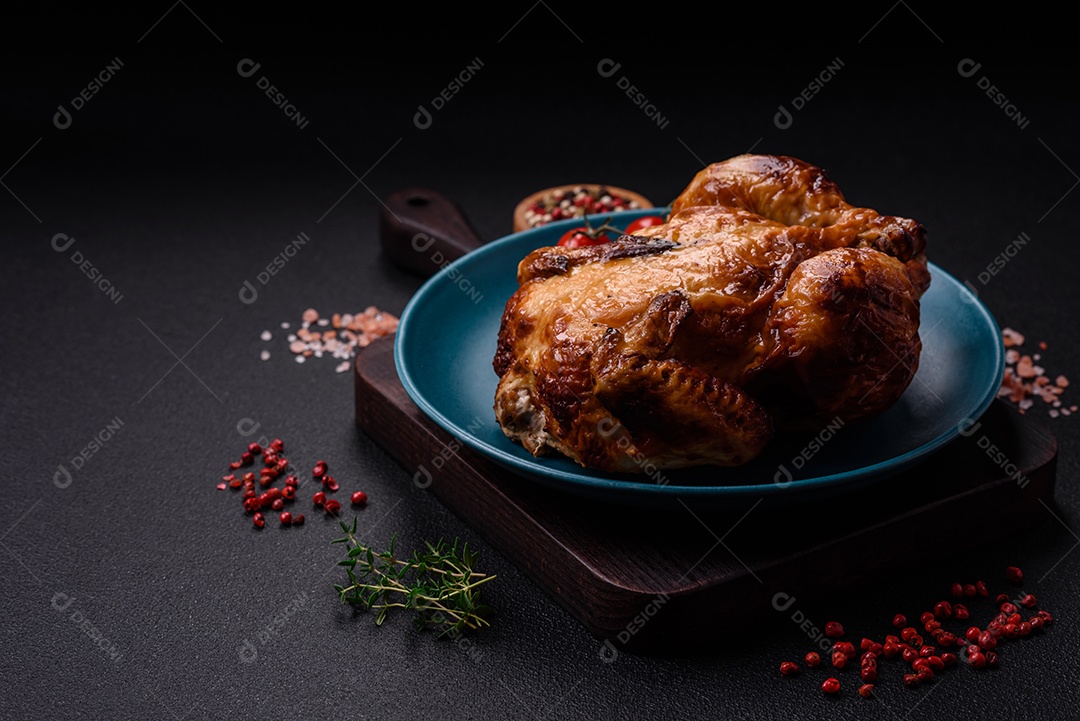 Frango assado inteiro delicioso e crocante com legumes, sal e especiarias sobre um fundo escuro de concreto
