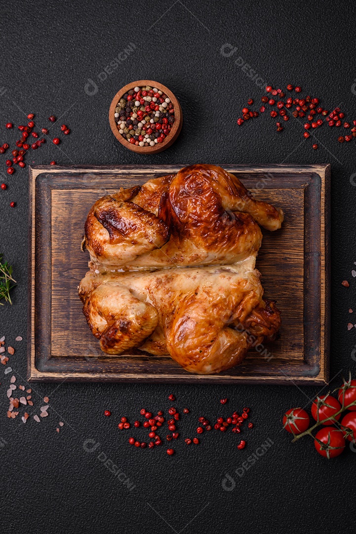 Frango assado inteiro delicioso e crocante com legumes, sal e especiarias sobre um fundo escuro de concreto