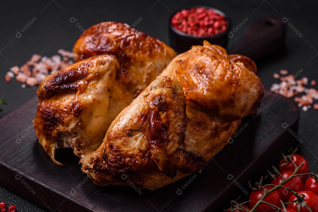 Frango assado inteiro delicioso e crocante com legumes, sal e especiarias sobre um fundo escuro de concreto