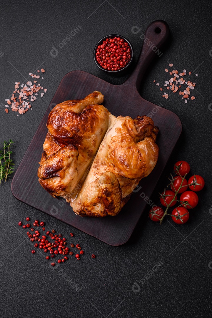 Frango assado inteiro delicioso e crocante com legumes, sal e especiarias sobre um fundo escuro de concreto