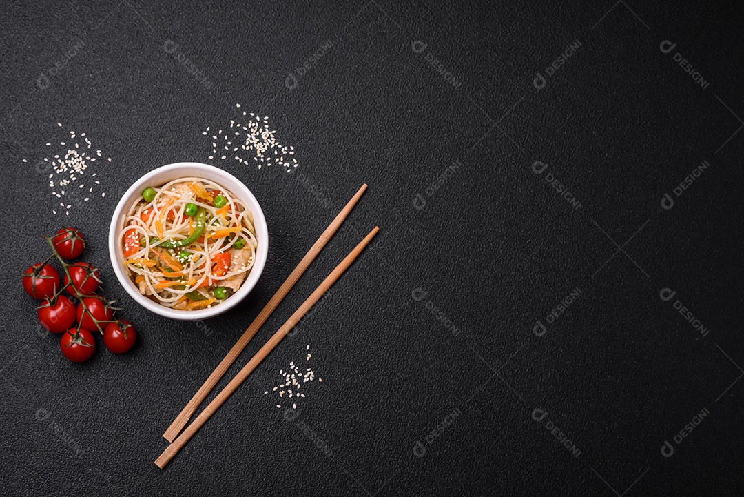 Saboroso prato de culinária asiática com macarrão de arroz, frango, aspargos, pimenta, sementes de gergelim e molho de soja em fundo escuro de concreto