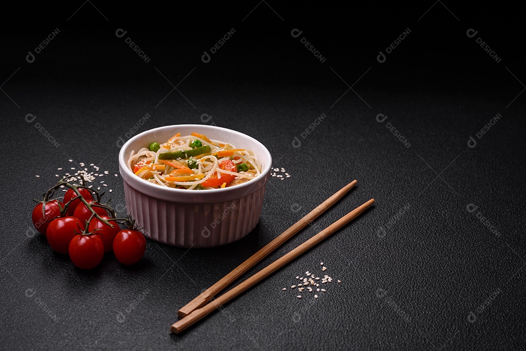 Saboroso prato de culinária asiática com macarrão de arroz, frango, aspargos, pimenta, sementes de gergelim e molho de soja em fundo escuro de concreto