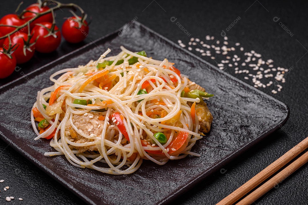 Saboroso prato de culinária asiática com macarrão de arroz, frango, aspargos, pimenta, sementes de gergelim e molho de soja em fundo escuro de concreto