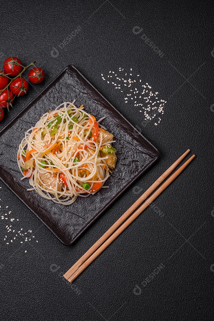 Saboroso prato de culinária asiática com macarrão de arroz, frango, aspargos, pimenta, sementes de gergelim e molho de soja em fundo escuro de concreto