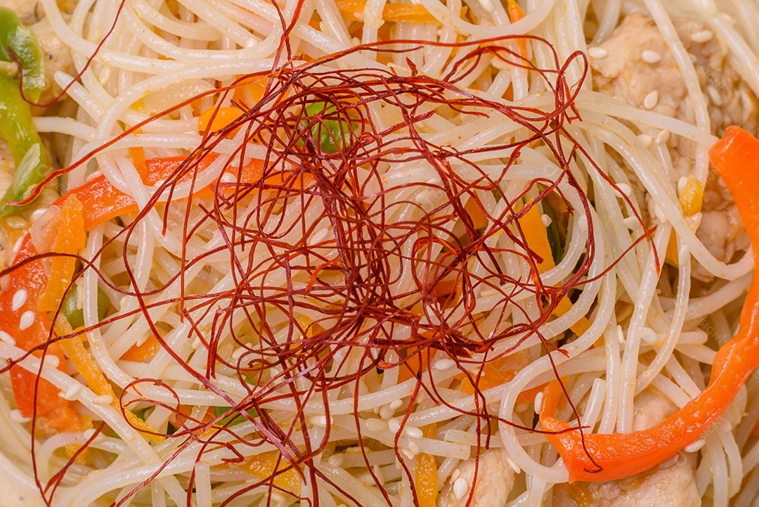 Saboroso prato de culinária asiática com macarrão de arroz, frango, aspargos, pimenta, sementes de gergelim e molho de soja em fundo escuro de concreto