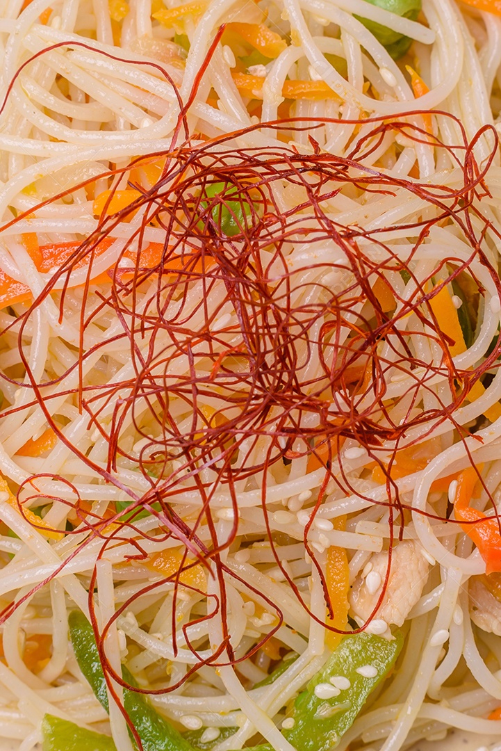 Saboroso prato de culinária asiática com macarrão de arroz, frango, aspargos, pimenta, sementes de gergelim e molho de soja em fundo escuro de concreto