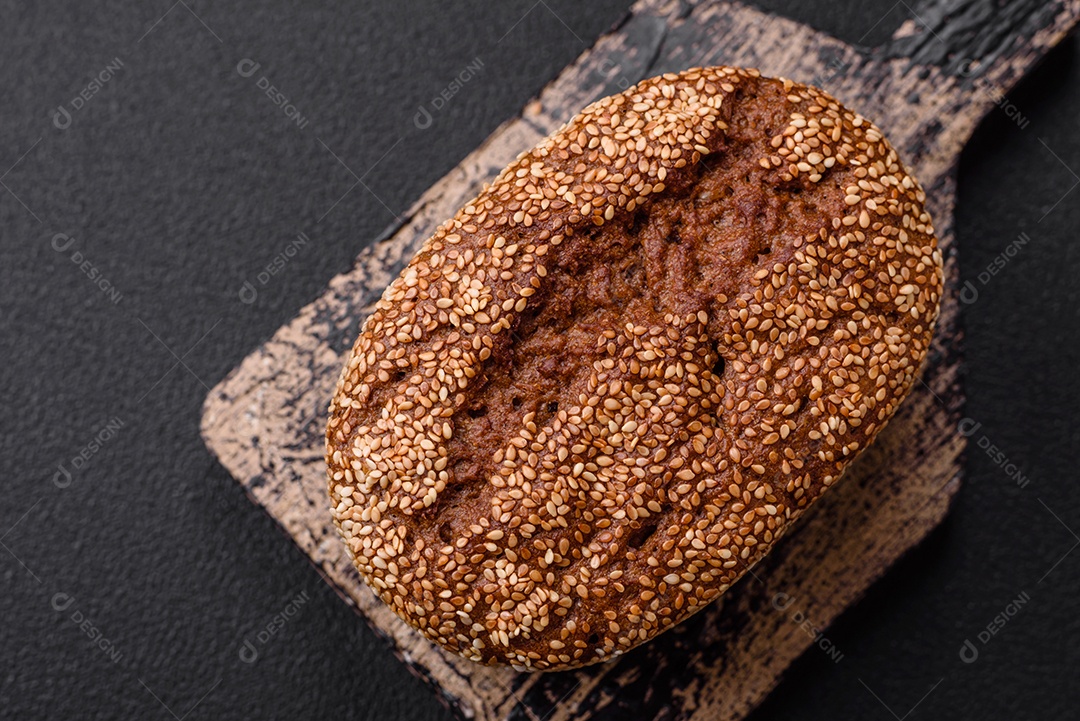 Delicioso pão integral crocante fresco com sementes e grãos sobre um fundo escuro de concreto