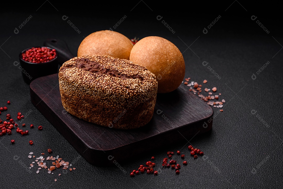 Delicioso pão redondo branco crocante fresco com sementes e grãos sobre um fundo escuro de concreto