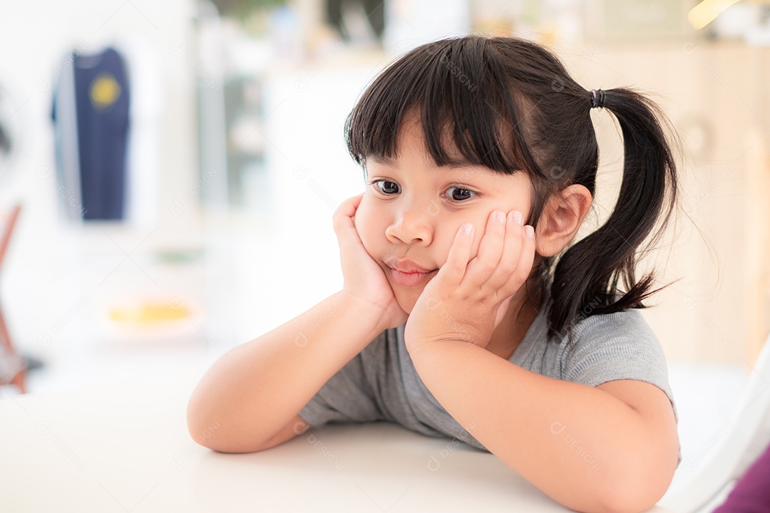 Linda menina asiática sentada com a mão no queixo e sorrindo enquanto espera para comer em uma mesa em um restaurante.