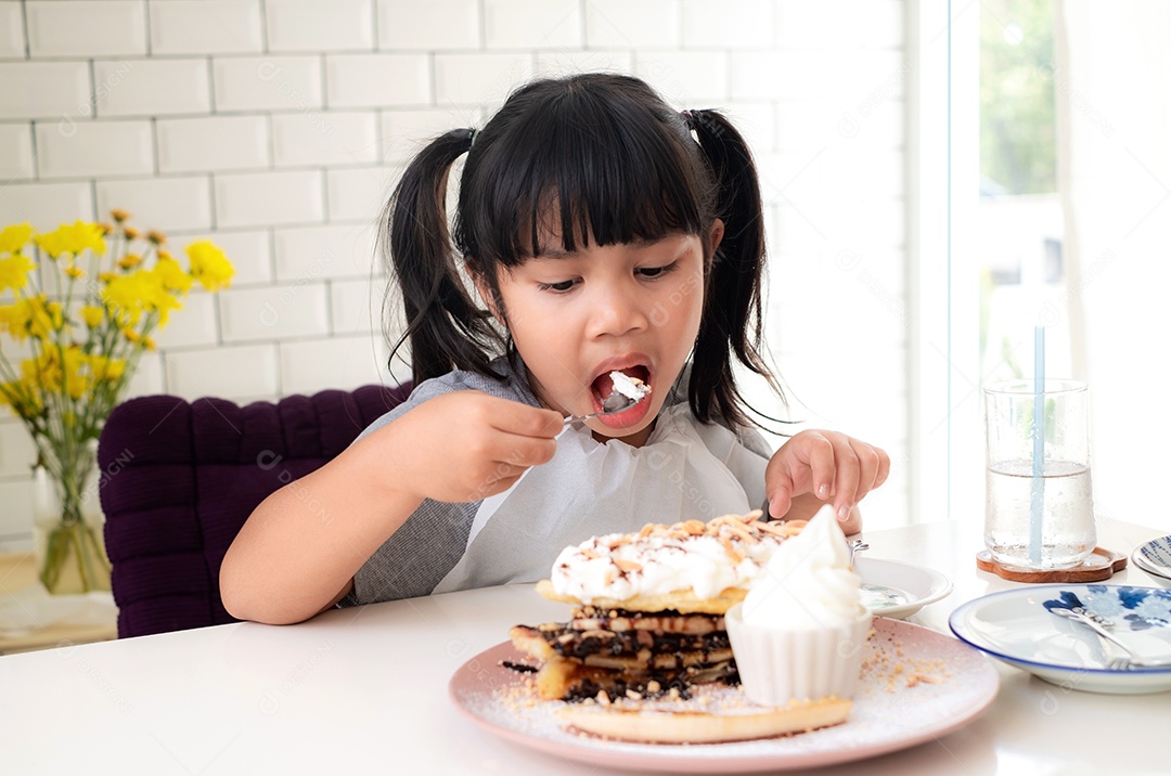 Linda garota asiática está comendo sobremesas deliciosas na mesa de um café.