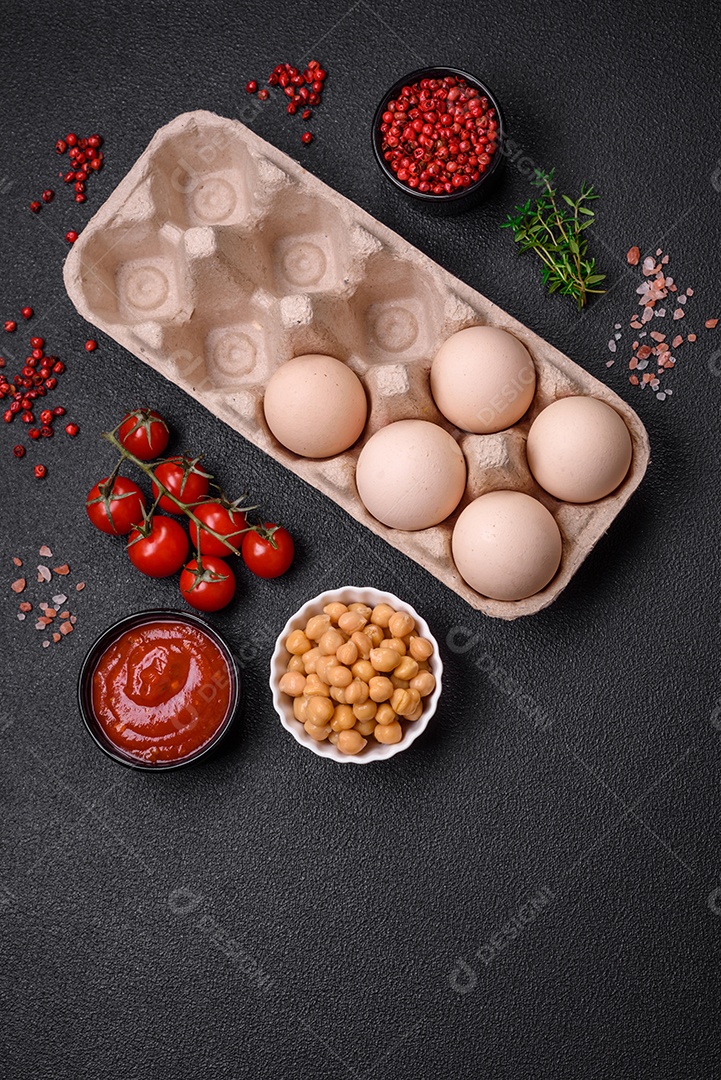 Ovos de galinha crus em uma caixa, tomate cereja, grão de bico, especiarias, sal e ervas. Ingredientes para um café da manhã delicioso e nutritivo