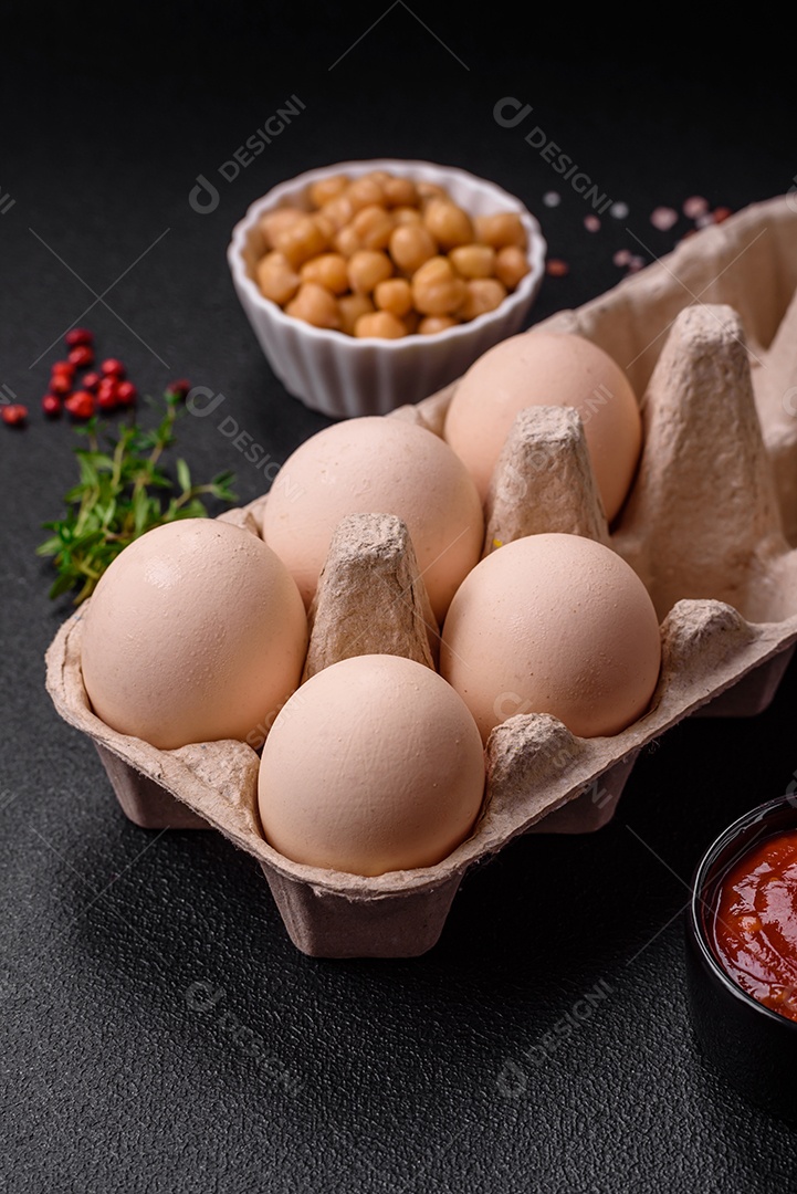 Ovos de galinha crus em uma caixa, tomate cereja, grão de bico, especiarias, sal e ervas. Ingredientes para um café da manhã delicioso e nutritivo