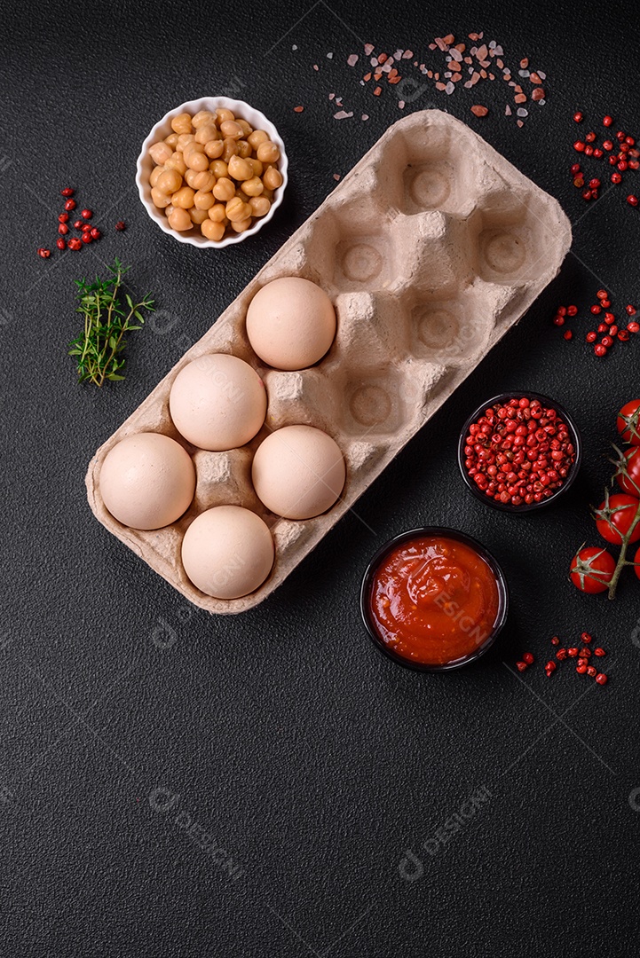 Ovos de galinha crus em uma caixa, tomate cereja, grão de bico, especiarias, sal e ervas.