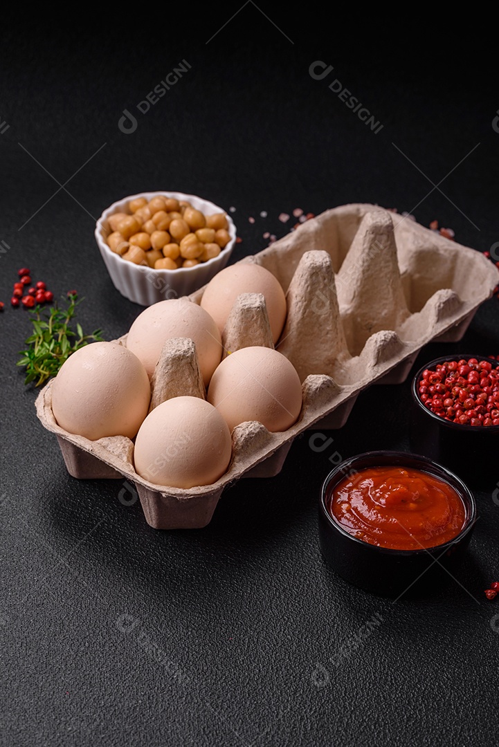 Ovos de galinha crus em uma caixa, tomate cereja, grão de bico, especiarias, sal e ervas.