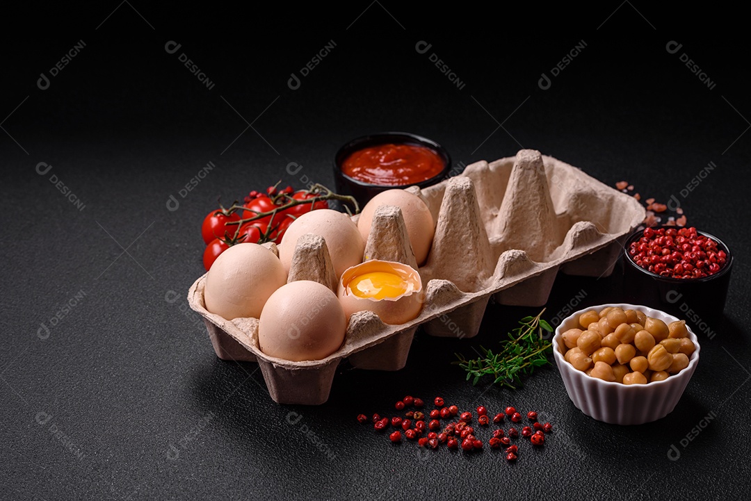 Ovos de galinha crus em uma caixa, tomate cereja, grão de bico, especiarias, sal e ervas.