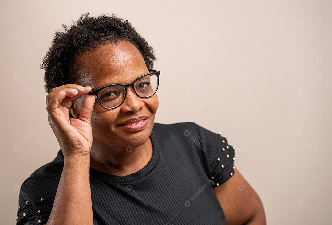 Mulher de meia idade colocando os óculos e sorrindo em fundo pastel.