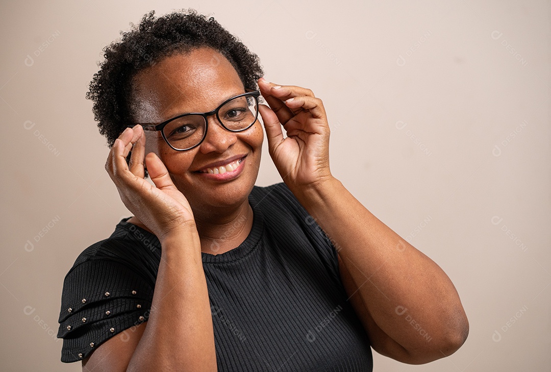 Mulher de meia idade segurando os óculos e sorrindo em fundo pastel.