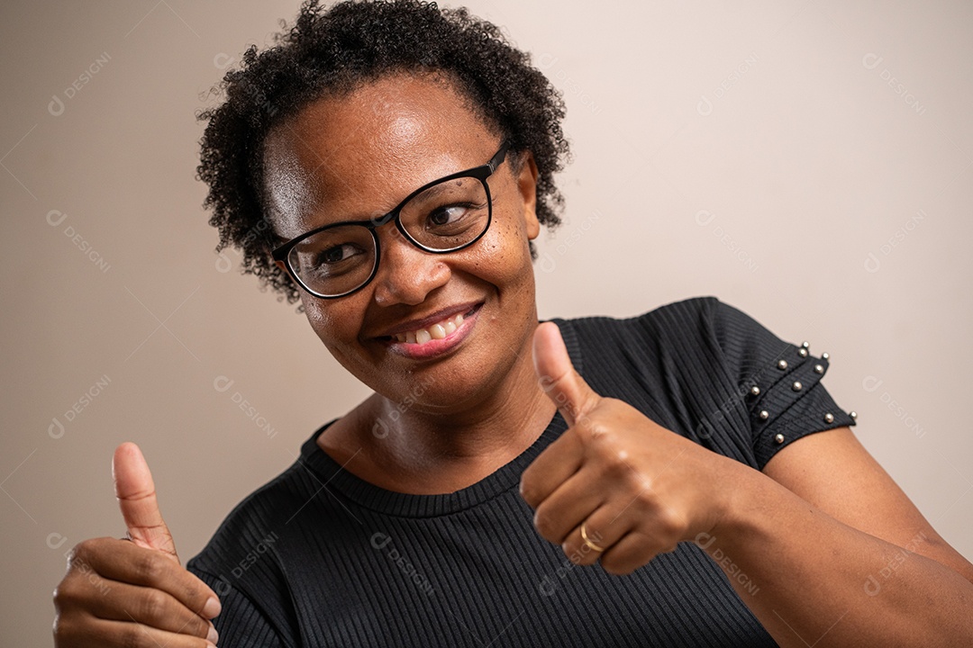 Mulher negra de óculos e sorrindo com polegares para cima em fundo pastel.
