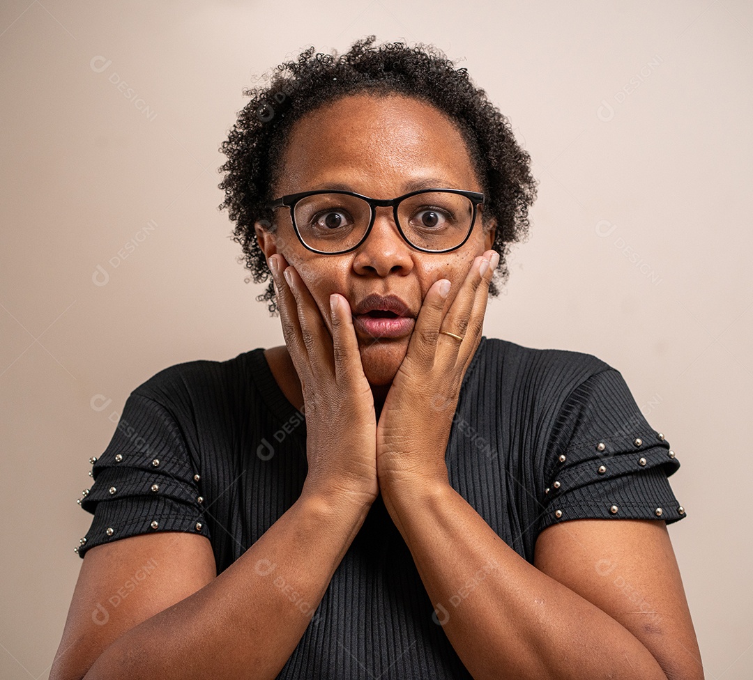 Mulher negra com as mãos no rosto e expressão de surpresa em fundo pastel.