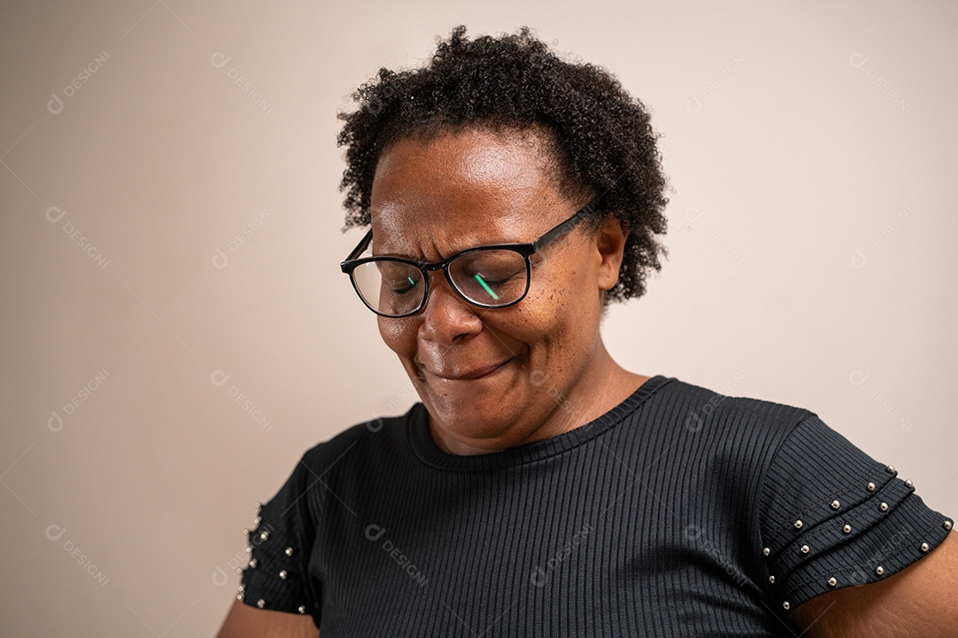 Mulher negra olhando para baixo com os olhos fechados com expressão triste em fundo pastel.