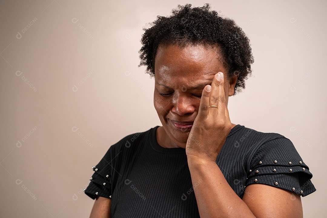 Mulher negra com a mão nos olhos chorando em fundo pastel.