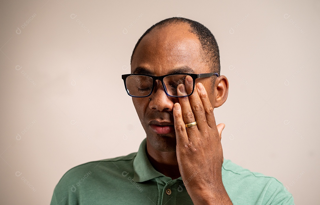 Homem coça o olho sob os óculos em um fundo pastel.