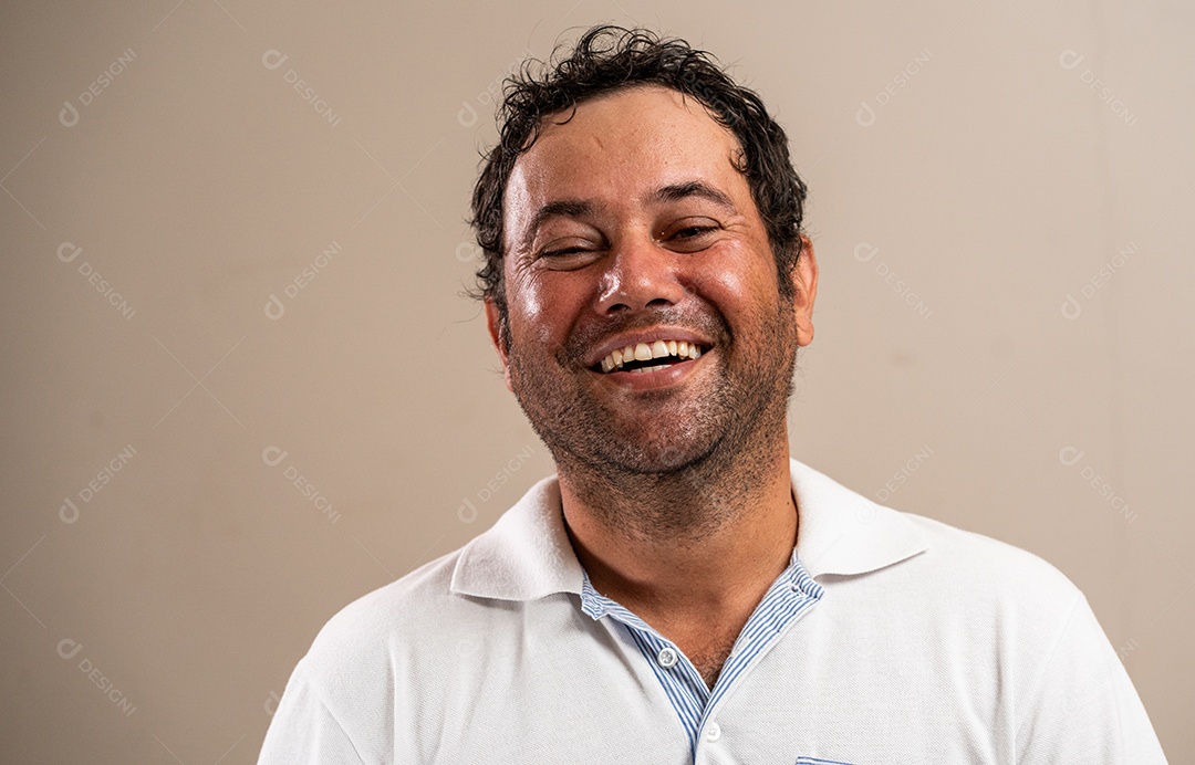 Homem com barba por fazer sorrindo com os olhos fechados em fundo pastel.
