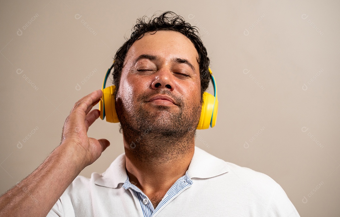 Homem com barba por fazer usando fones de ouvido em fundo pastel.