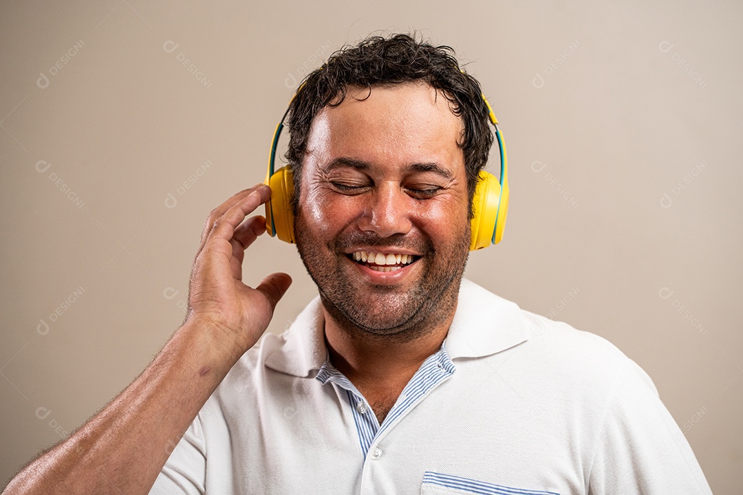Homem com barba por fazer usando fones de ouvido em fundo pastel.