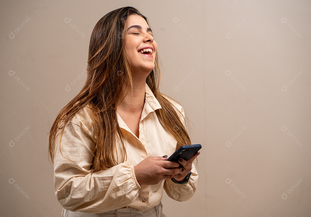 Rindo jovem segurando smartphone em fundo pastel.