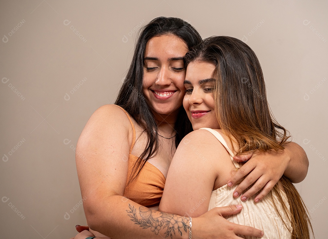 Mulheres jovens sorridentes, abraçando-se em fundo pastel.