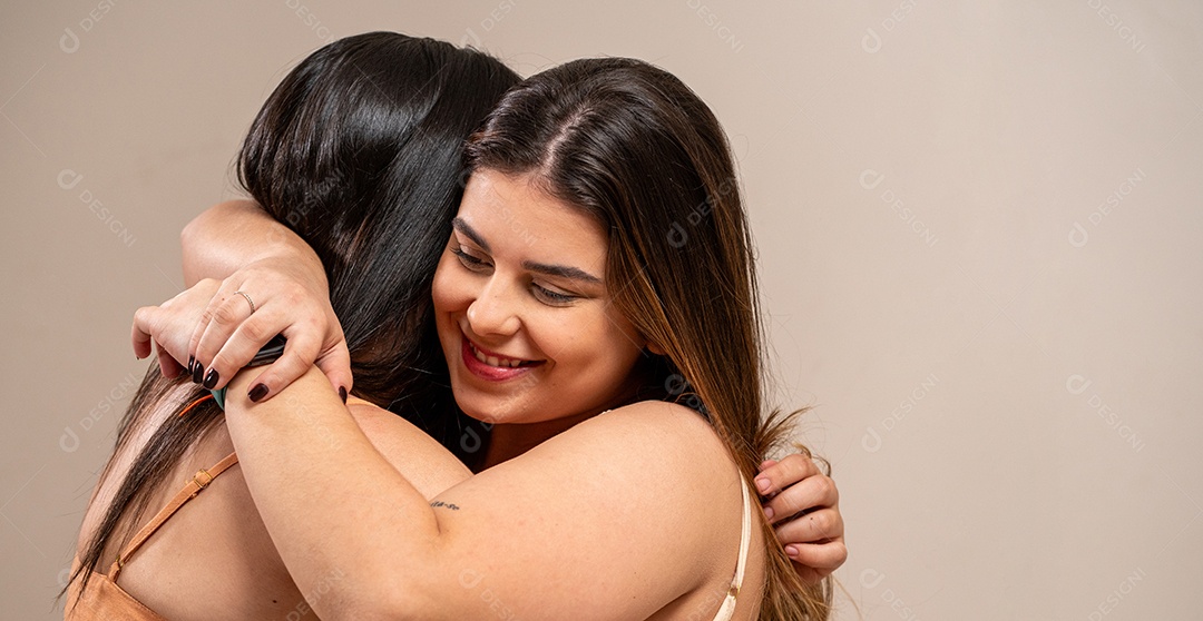 Mulheres jovens sorridentes, abraçando-se em fundo pastel.