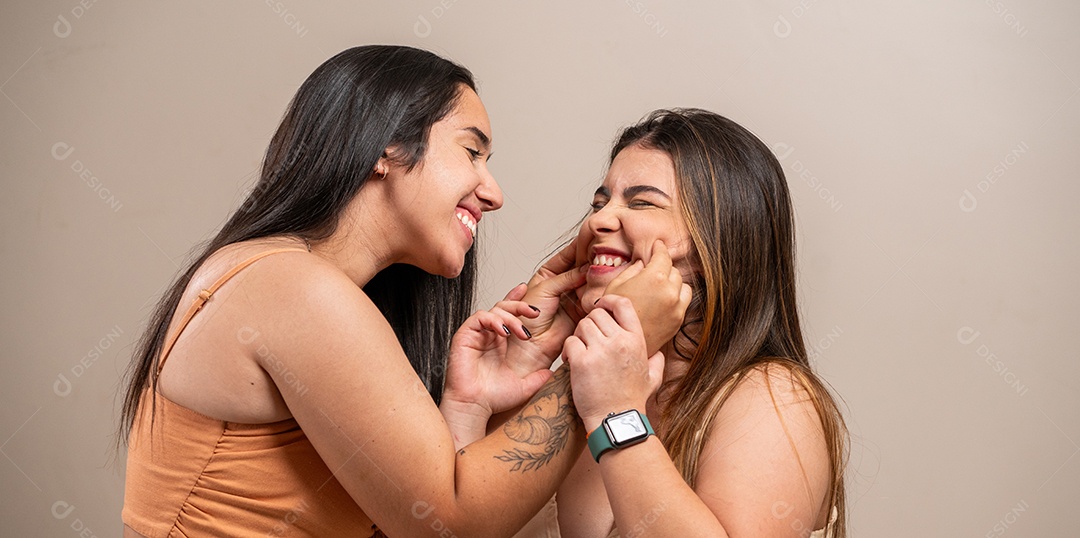 Casal de mulheres jovens beijando em fundo pastel.
