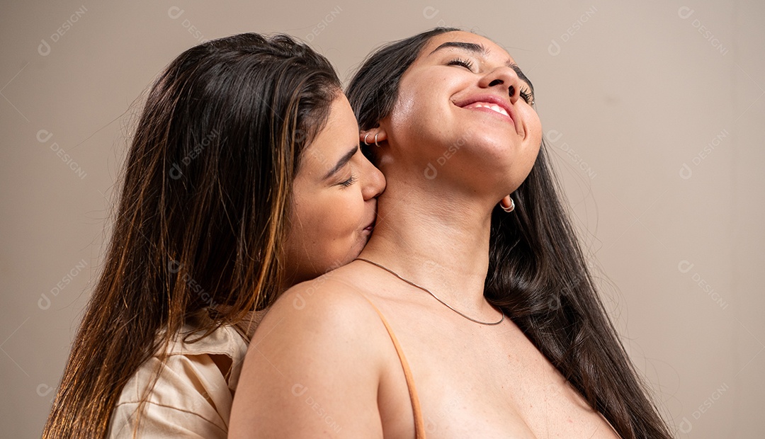 Jovem beijando o pescoço da namorada em fundo pastel.