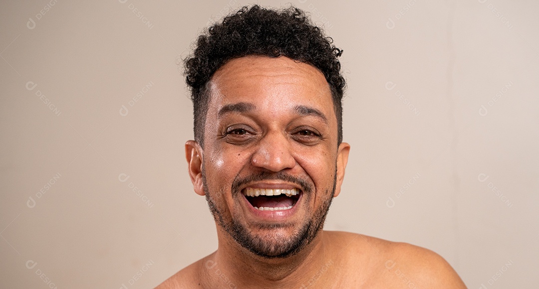 Retrato aproximado. Homem moreno sem camisa rindo em fundo pastel.