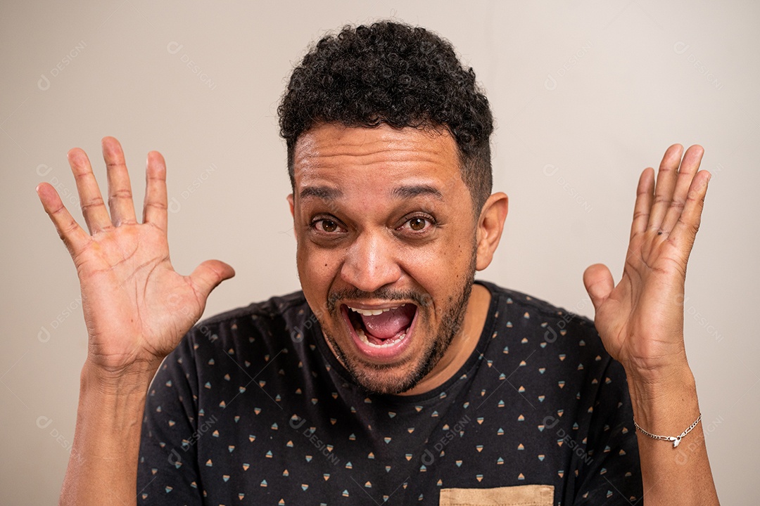 Homem moreno com as mãos para cima e expressão espantada em fundo pastel.