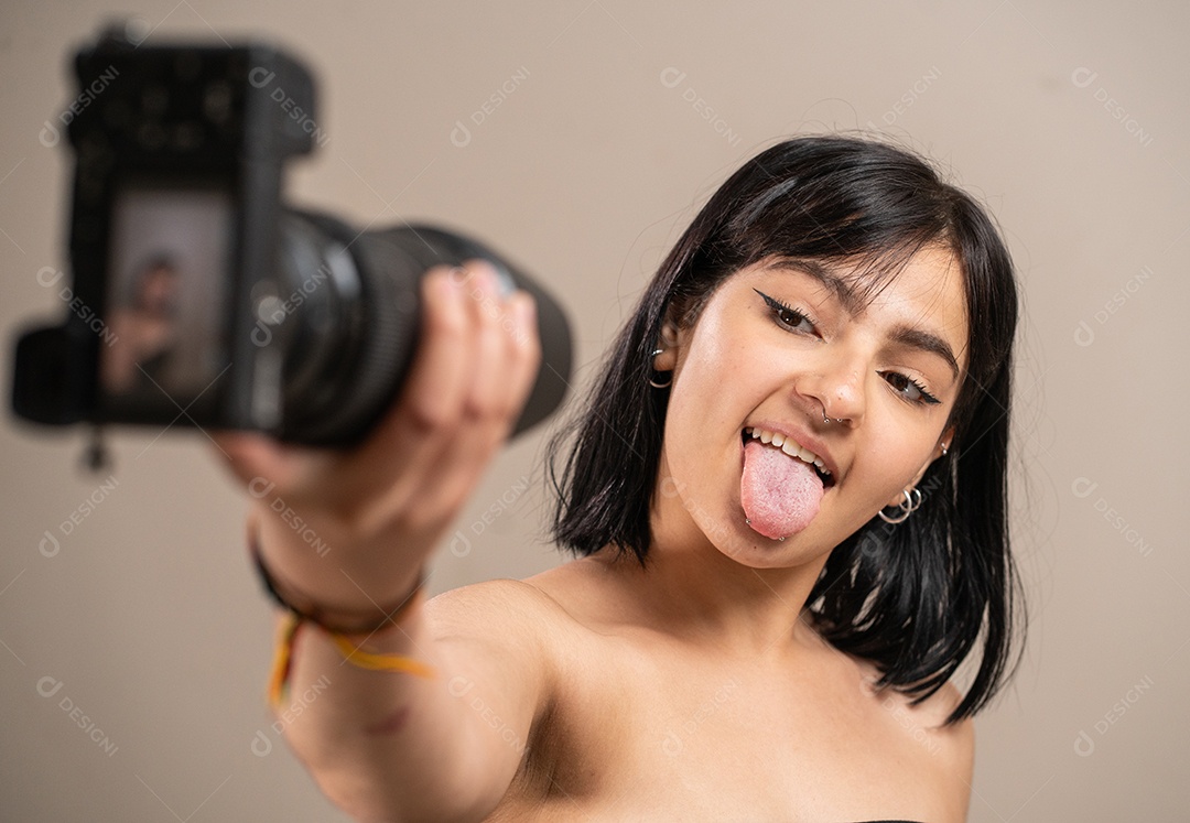 Menina segurando uma câmera tirando uma selfie mostrando a língua em um fundo pastel